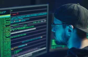 A cybersecurity expert inspecting lines of code on multiple monitors in a dimly lit office.